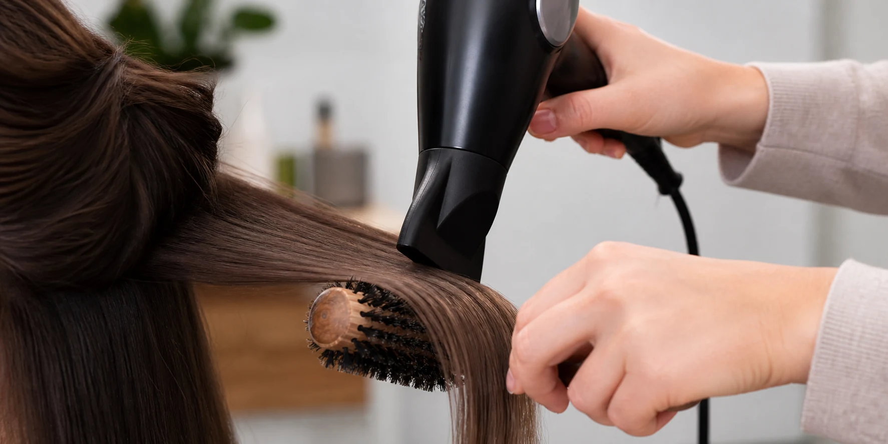 Two hand round brush blowout technique showing dryer nozzle angled along a section of hair